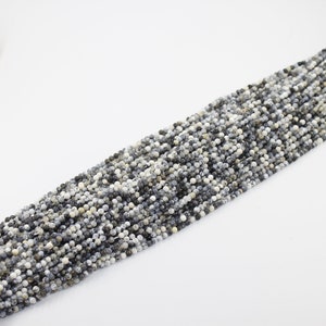 May include: A strand of small, round, white and gray gemstone beads. The beads have a speckled pattern and are strung on a thin thread.