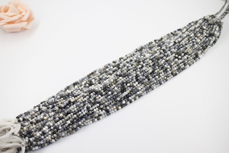 May include: A strand of small, round, white and gray gemstone beads. The beads have a speckled pattern and are strung on a thin thread.