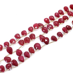 Könnte beinhalten: Eine Strähne roter Edelsteinperlen in Tropfenform. Die Perlen sind auf einem goldenen Draht aufgefädelt.