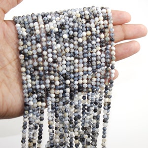 May include: A strand of white and black speckled round gemstone beads. The beads are approximately 4mm in diameter and are strung on a clear elastic cord.