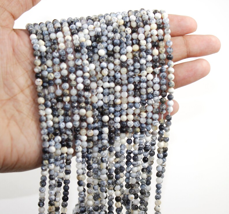 May include: A strand of white and black speckled round gemstone beads. The beads are approximately 4mm in diameter and are strung on a clear elastic cord.
