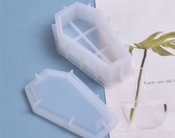 May include: Two white silicone moulds shaped like a coffin. The moulds are open and ready to be used to create resin crafts.