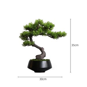 K&ouml;nnte beinhalten: Ein k&uuml;nstlicher Bonsai-Baum mit leuchtend gr&uuml;nem Laub und einem strukturierten braunen Stamm, gepflanzt in einem schwarzen, konisch zulaufenden Keramiktopf. Die Pflanze ist 35 cm hoch und 30 cm breit, wie durch die sichtbaren Ma&szlig;linien dargestellt.
