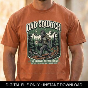 Può includere: Una maglietta arancione con una grafica di una creatura simile a Bigfoot che tiene una tazza di caffè, con il testo "DAD SQUATCH" e "THE ORIGINAL OUTDOORSMAN". Il design include montagne, alberi e il testo "DIGITAL FILE ONLY - INSTANT DOWNLOAD".