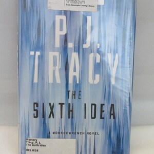 May include: A hardcover book titled The Sixth Idea by P.J. Tracy, featuring a blue and white abstract vertical streak cover design. The book includes a white library sticker at the top reading Officially Withdrawn and a label at the bottom.