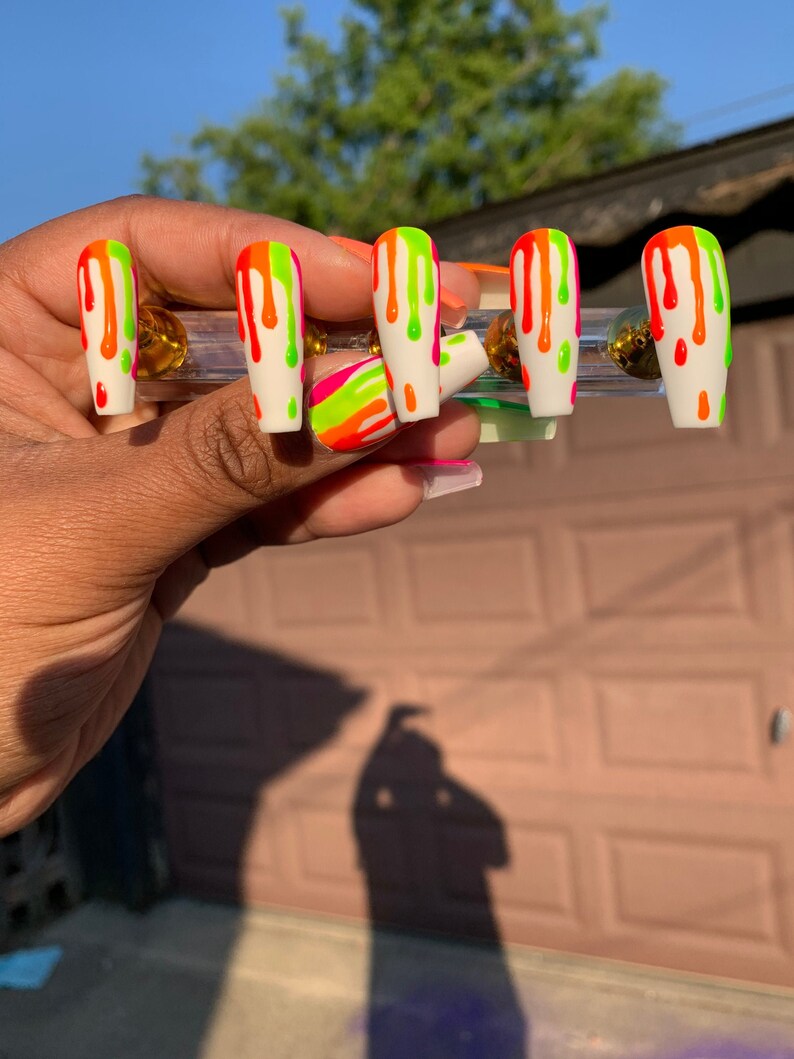 May include: Set of five white press-on nails with a drip design. The nails are decorated with neon green, orange, and pink paint.