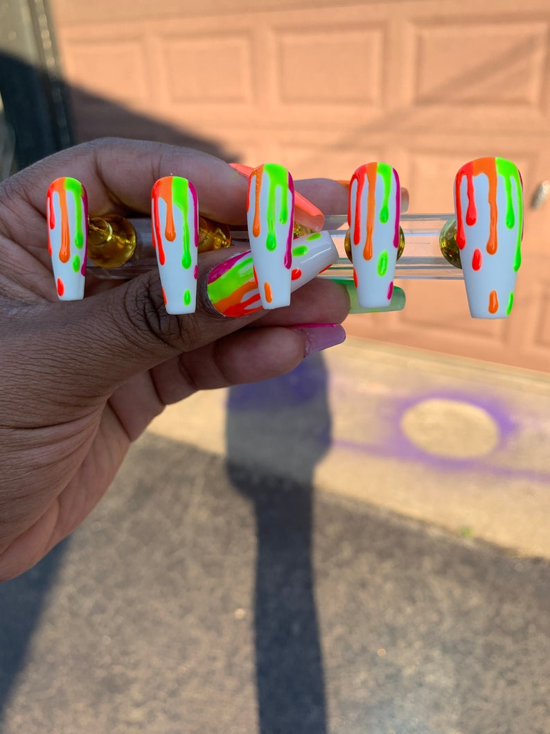 May include: Set of five white press-on nails with a drip design. The nails are painted with bright neon green, orange, and pink colours.