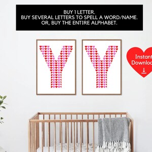 May include: Two framed prints of the letter "Y", each made up of red and pink heart shapes on a white background. The prints are displayed on a white wall, with a cot and plant visible below. Text above reads: "BUY 1 LETTER. BUY SEVERAL LETTERS TO SPELL A WORD/NAME. OR, BUY THE ENTIRE ALPHABET."