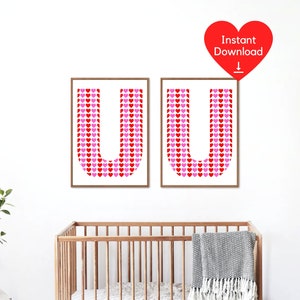 May include: Two framed prints, each showing the letter 'U' made of red and pink hearts. The prints are in wooden frames and hang on a white wall. A red heart graphic with 'Instant Download' is above the prints. A cot is in the foreground.