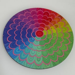 May include: A circular mouse mat with a bright, rainbow-coloured design. The pattern features concentric circles of colour, ranging from blue to red, with pink outlines. A computer accessory.