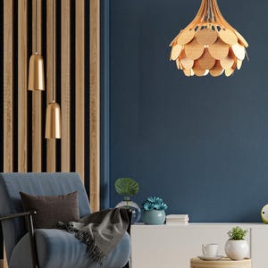 May include: A modern living room featuring a blue armchair, a wooden accent wall, and a unique wooden pendant light. The light fixture has a layered, petal-like design. Two gold pendant lights hang from the ceiling. A small wooden side table holds a cup and plant.