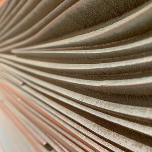 May include: Close-up of a textured, light gray wall with a series of curved, horizontal lines. The lines create a wave-like pattern.