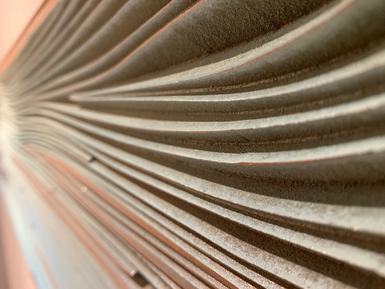 May include: Close-up of a textured, light gray wall with a series of curved, horizontal lines. The lines create a wave-like pattern.