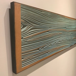 May include: A framed abstract artwork with a wood-like pattern in shades of blue and brown. The artwork is mounted on a wall.