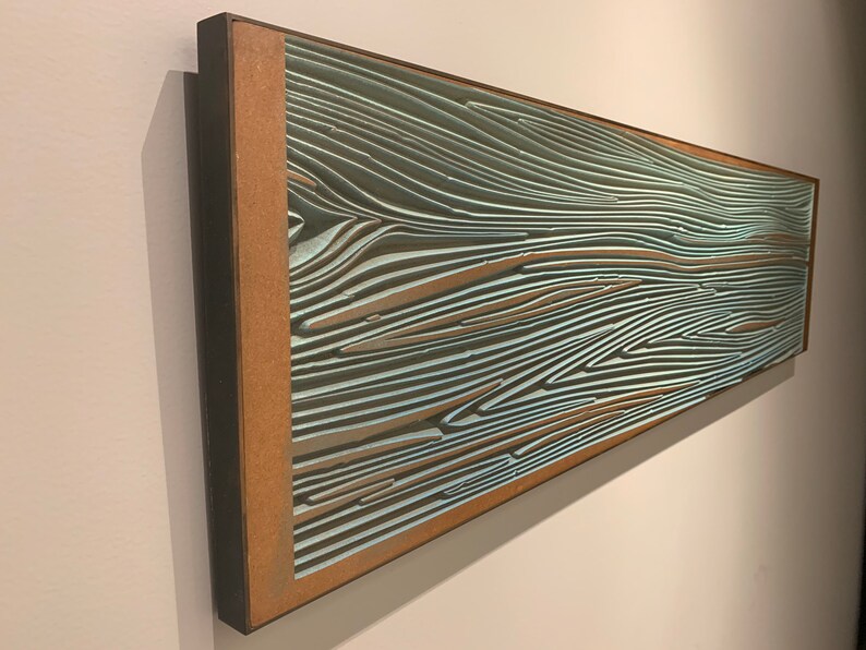 May include: A framed abstract artwork with a wood-like pattern in shades of blue and brown. The artwork is mounted on a wall.