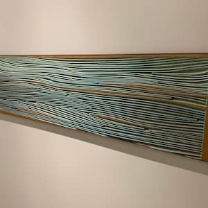 May include: A long, rectangular mirror with a wooden frame. The mirror's surface is covered in a pattern of thin, wavy lines in shades of brown, blue, and white.