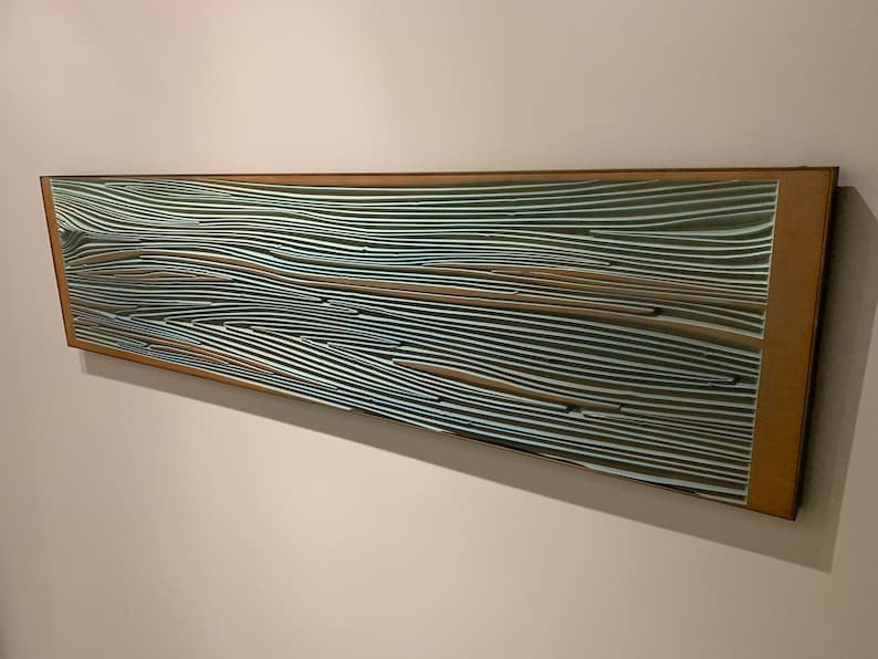 May include: A long, rectangular mirror with a wooden frame. The mirror's surface is covered in a pattern of thin, wavy lines in shades of brown, blue, and white.
