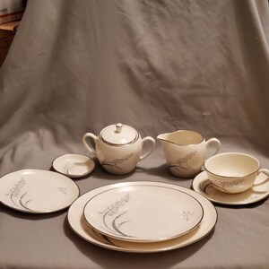 May include: A set of white porcelain teacups and saucers with a delicate floral design in silver. The set includes a sugar bowl and creamer.