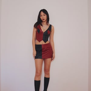 May include: A woman wearing a black and red leather skirt and top with a heart and diamond design. She is wearing black platform boots.