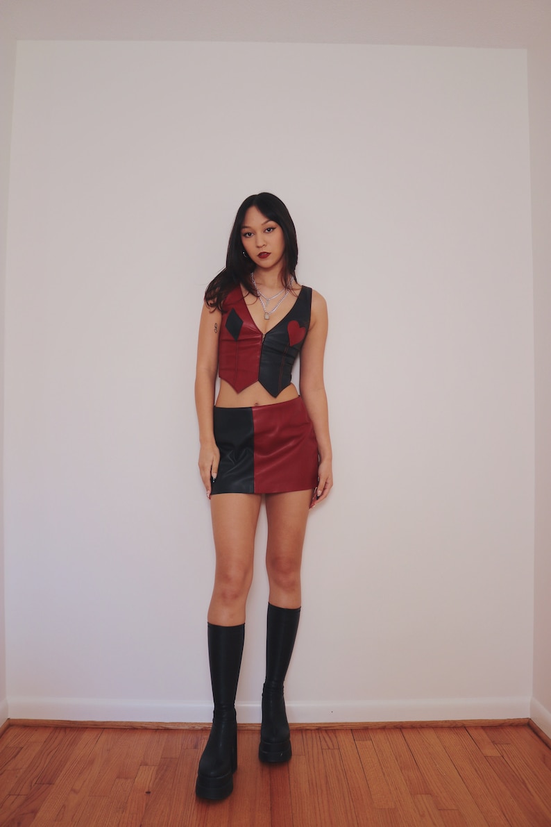 May include: A woman wearing a black and red leather skirt and top with a heart and diamond design. She is wearing black platform boots.