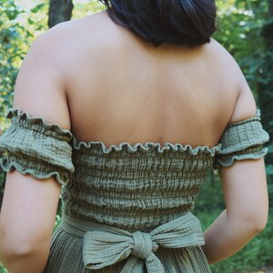 Op de afbeelding: Een groene off-shoulder jurk met een gerimpelde halslijn en een strik die aan de achterkant is gebonden.