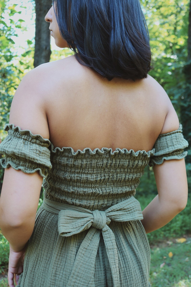 Op de afbeelding: Een groene off-shoulder jurk met een gerimpelde halslijn en een strik die aan de achterkant is gebonden.
