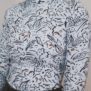 May include: A long-sleeved, light blue turtleneck shirt with a black and brown abstract print. The print features stylized leaves, flowers, and swirls.