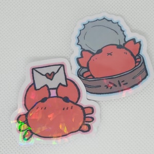 May include: Two holographic stickers featuring cartoon crabs. One crab is holding a letter with a heart on it. The other crab is inside a can with a lid on top. The can has the word "蟹" written on it.