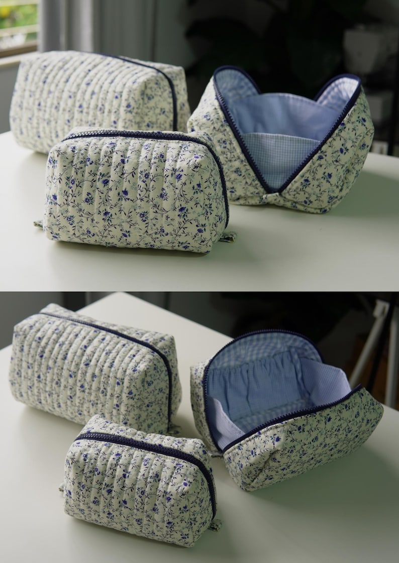 May include: A set of three quilted pouches featuring a white fabric with a blue floral pattern and dark blue zips. The pouches have a rectangular shape with vertical stitching and a light blue gingham interior lining.