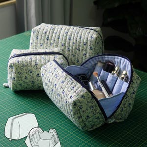 May include: Three quilted fabric pouches with a blue floral pattern on a white background, featuring dark blue zippers. One pouch is open, revealing internal pockets holding cosmetic items. A line drawing shows the pouch structure. Text reads: 3 SIZES, DIFFICULTY, A4, A0, US LETTER.