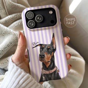 May include: A smartphone case featuring a vertical lavender and white striped pattern with a central illustration of a black and tan Doberman dog wearing a light pink collar. The name Rhea is printed in a cursive script next to the dog's head.