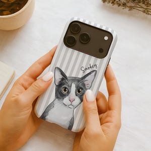 May include: A smartphone case featuring a light gray and white vertical striped pattern. The case displays a detailed illustration of a gray and white cat with large eyes and the name Smokey written in cursive script above the cat's head.