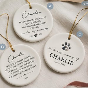 May include: Three white ceramic round ornaments with gold hanging strings. Each features black printed text and graphics, including the name Charlie, memorial quotes, dates, and paw print designs. The ornaments are labeled with letters A, B, and C.