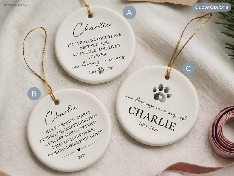 May include: Three white ceramic round ornaments with gold hanging strings. Each features black printed text and graphics, including the name Charlie, memorial quotes, dates, and paw print designs. The ornaments are labeled with letters A, B, and C.