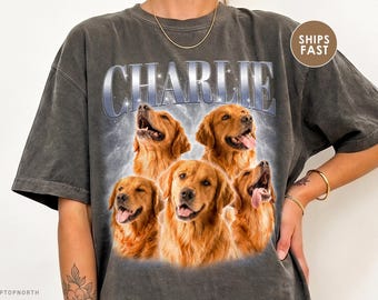 Puede incluir: Una camiseta gris carbón de manga corta con un estampado gráfico de cinco perros golden retriever. La palabra CHARLIE está impresa en letras grandes de tono metálico sobre los perros, contra un fondo claro y nublado.