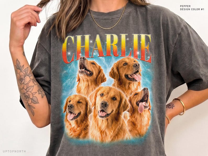 May include: A charcoal gray t-shirt featuring a graphic print of five golden retriever dogs arranged in a cluster. Above the dogs, the name CHARLIE is printed in large, bold, orange and yellow gradient letters against a blue background.