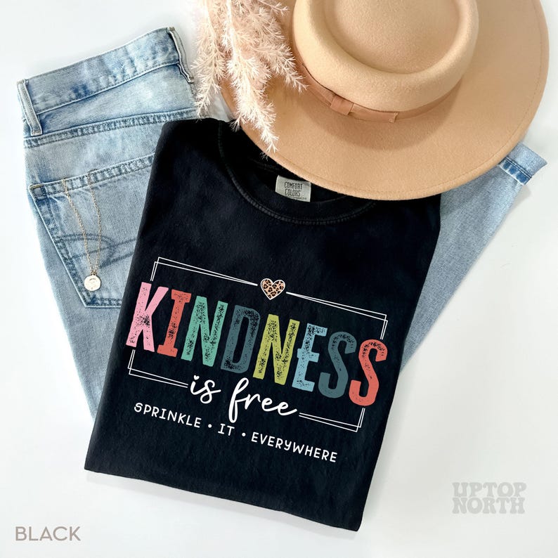 Pode incluir: Camiseta preta com um gr&aacute;fico de arco-&iacute;ris que diz "A gentileza &eacute; gratuita" e "Espalhe-a por toda parte".