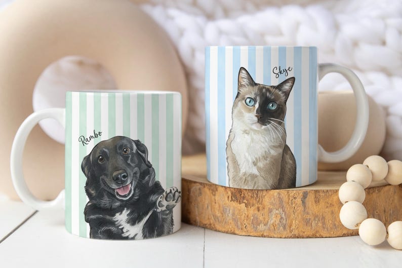 May include: Two white ceramic mugs featuring custom pet portraits. The left mug has a light green striped background with a black dog illustration labeled Rambo. The right mug has a light blue striped background with a cat illustration labeled Skye.