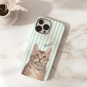 May include: A phone case featuring a cat illustration. The case has a mint green and white striped background. The cat is brown and tan with a white collar. The name "Hazel" is written in script on the case.