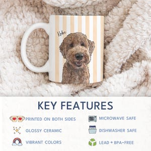 May include: A white ceramic mug featuring a vertical light orange and white striped pattern with a detailed illustration of a brown curly-haired dog and the name Kobe printed in black script above the dog's head, with a white handle on the left.