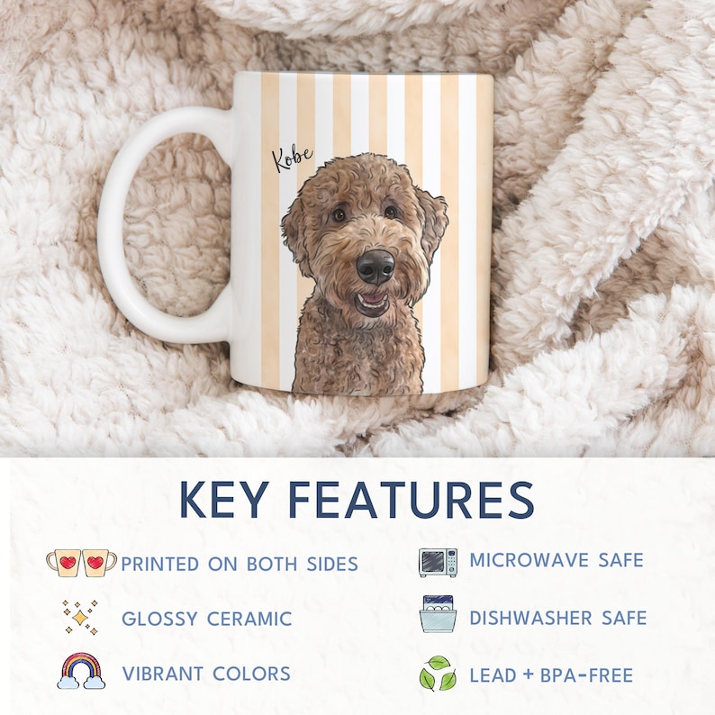 May include: A white ceramic mug featuring a vertical light orange and white striped pattern with a detailed illustration of a brown curly-haired dog and the name Kobe printed in black script above the dog's head, with a white handle on the left.