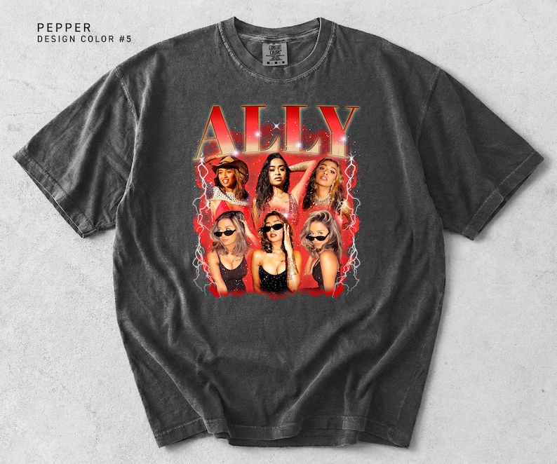 May include: A dark gray t-shirt featuring a graphic of the word "ALLY" in red, with a vintage-style design. The graphic includes images of six women. The shirt has a crew neck and short sleeves.