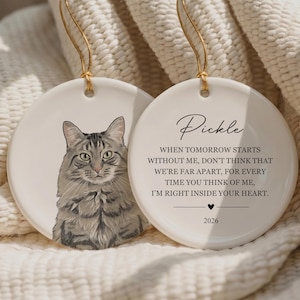 May include: Two round white ceramic ornaments with gold hanging strings. One features a detailed illustration of a grey tabby cat. The other displays the name Pickle, a memorial poem, a small heart icon, and the year 2026 in black text.