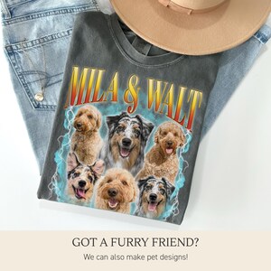 K&ouml;nnte beinhalten: Ein anthrazitfarbenes T-Shirt mit dem Text "MILA & WALT" in einer Retro-Schriftart und einem Blitzdesign. Das Shirt zeigt eine Collage von sechs verschiedenen Hunderassen. Ein beigefarbener Hut und blaue Jeans sind ebenfalls im Bild.