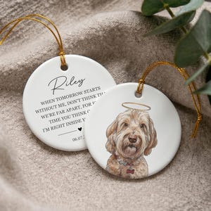 May include: Two round white ceramic ornaments with gold hanging strings. One features a hand-drawn illustration of a golden-colored dog with a halo. The other displays the name Riley and the text: When tomorrow starts without me, don't think we're far apart, for every time you think of me, I'm right inside your heart, with a date 06.07.2023.