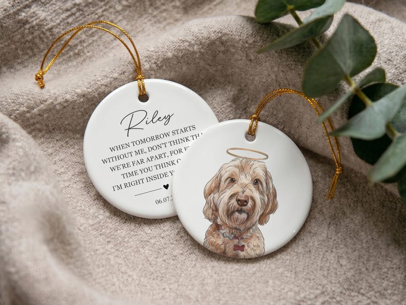 May include: Two round white ceramic ornaments with gold hanging strings. One features a hand-drawn illustration of a golden-colored dog with a halo. The other displays the name Riley and the text: When tomorrow starts without me, don't think we're far apart, for every time you think of me, I'm right inside your heart, with a date 06.07.2023.