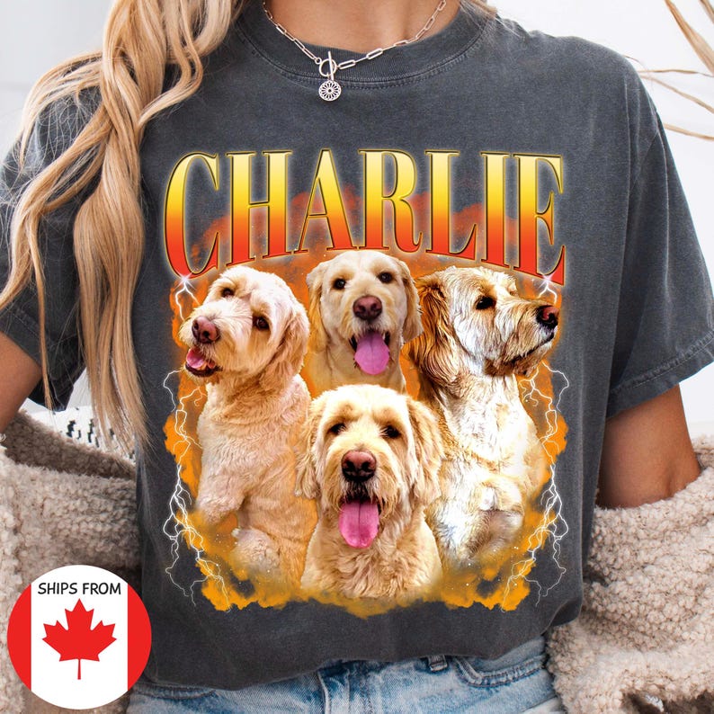 Pu&ograve; includere: T-shirt grigio scuro con il nome "CHARLIE" in un font retr&ograve; sopra una grafica di quattro cani. I cani sono di varie tonalit&agrave; di beige e oro, con alcune lingue visibili. Grafiche di fulmini circondano i cani.