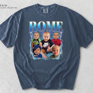 May include: Denim blue t-shirt with a graphic design featuring the word "ROME" in a blue and gold font, with images of five babies. The shirt has a vintage, faded look.