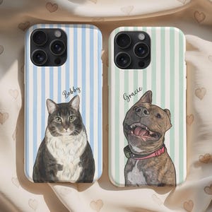 May include: Two phone cases featuring custom pet portraits. The left case has a blue striped background with a brown and white cat labeled Bobby. The right case has a green striped background with a brown brindle dog wearing a pink collar labeled Gracie.