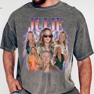 May include: A charcoal gray short-sleeve t-shirt featuring a graphic print with the name JULIE in a gradient font. The design includes multiple photographic portraits of a person, surrounded by a purple lightning effect and stars.